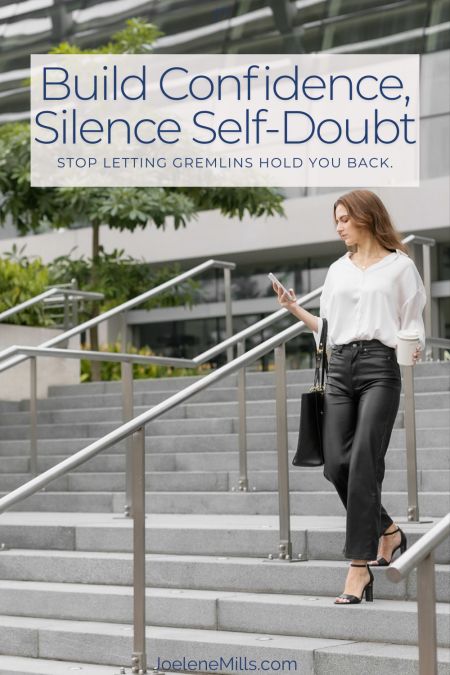 Woman walking down a set of stairs outside an office building, lookingat her phone with the words build confidence silence self-doubt