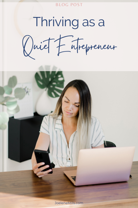 A business woman looking at her phone, while at her desk with her laptop open in front of her. The words "thriving as a quiet entrepreneur" above her