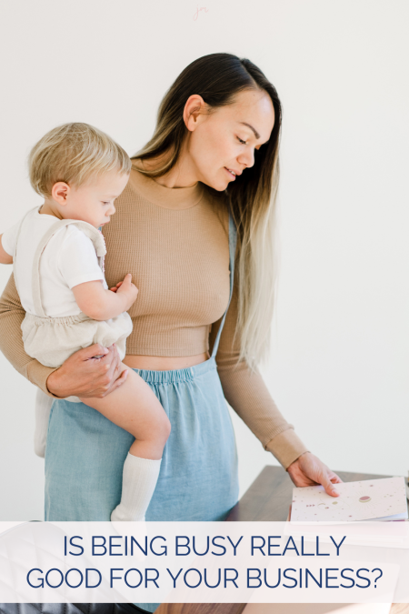 Business woman holding her baby while working at her desk with the words "is being busy really good for business?"