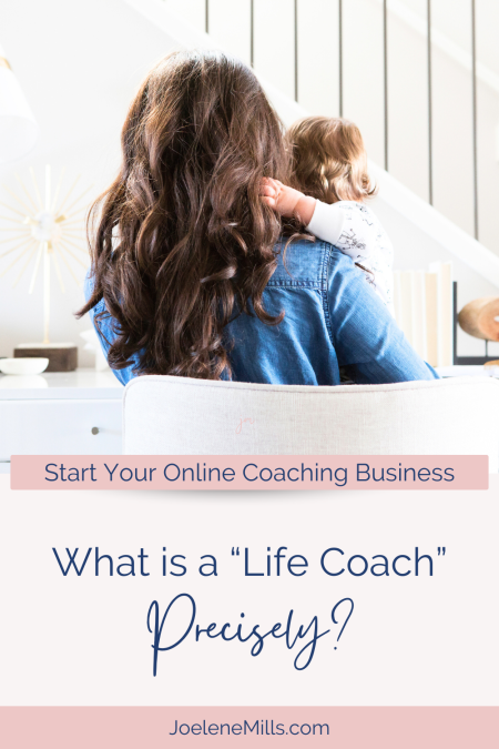 A photo of the back of a woman sitting at her desk holding her toddler, with the words "What is a "life coach" precisely?"